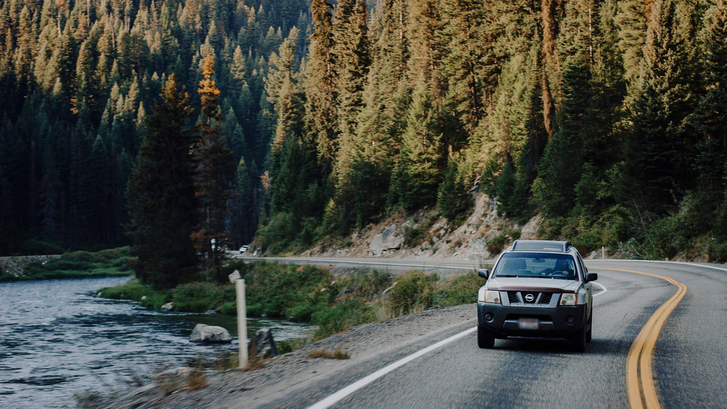 a car driving down a winding road running alongside a river, surrounded by trees