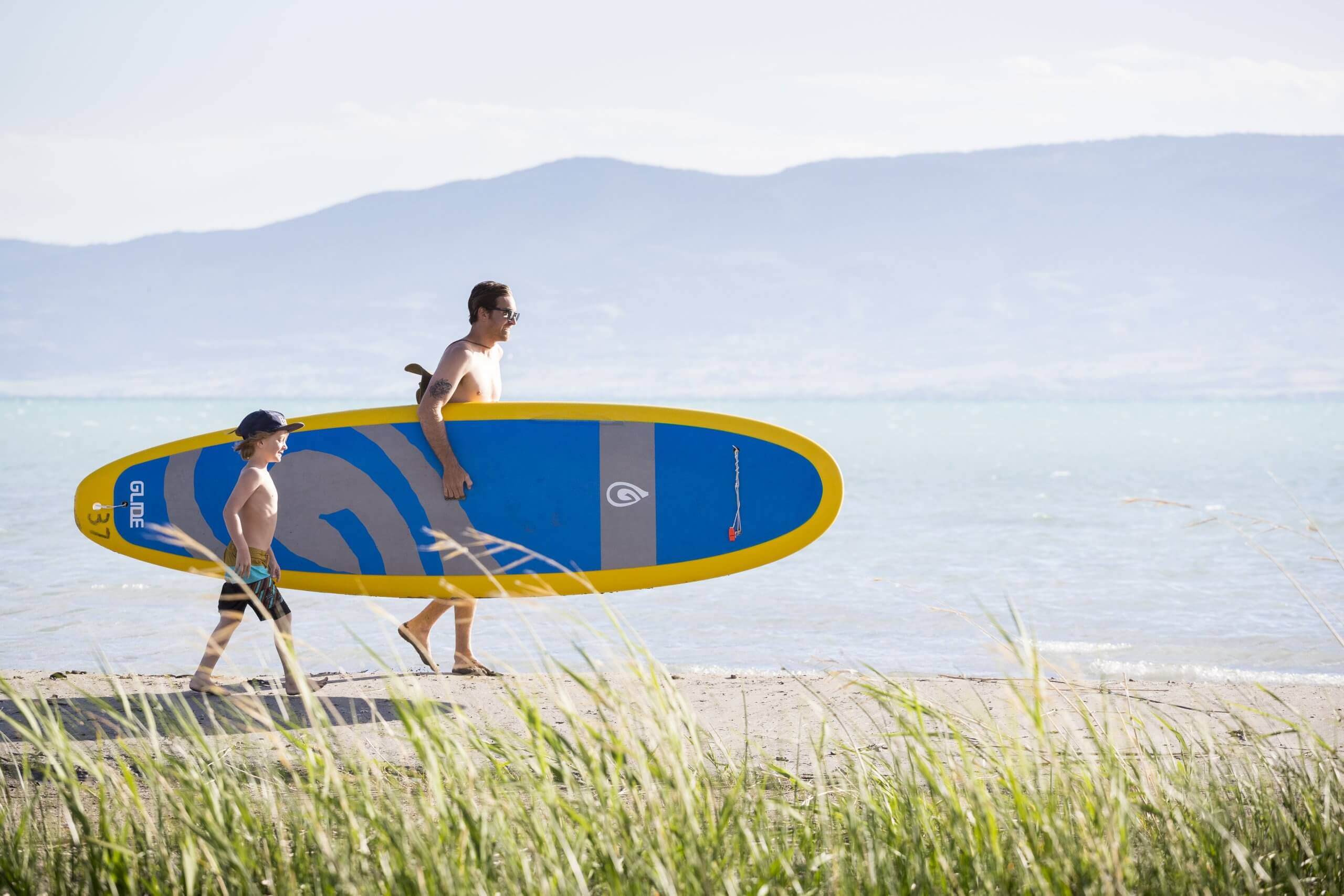 A father and son walking to the lake with their paddle board.