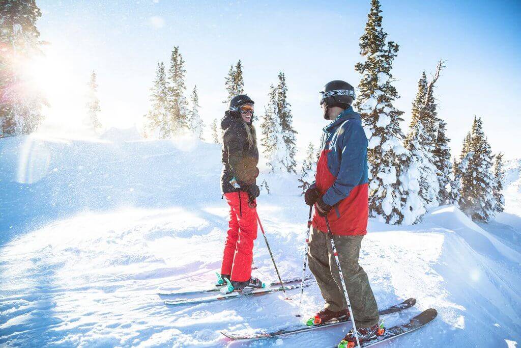 A couple facing each other on the powder in front of trees at Pomerelle Mountain Resort.