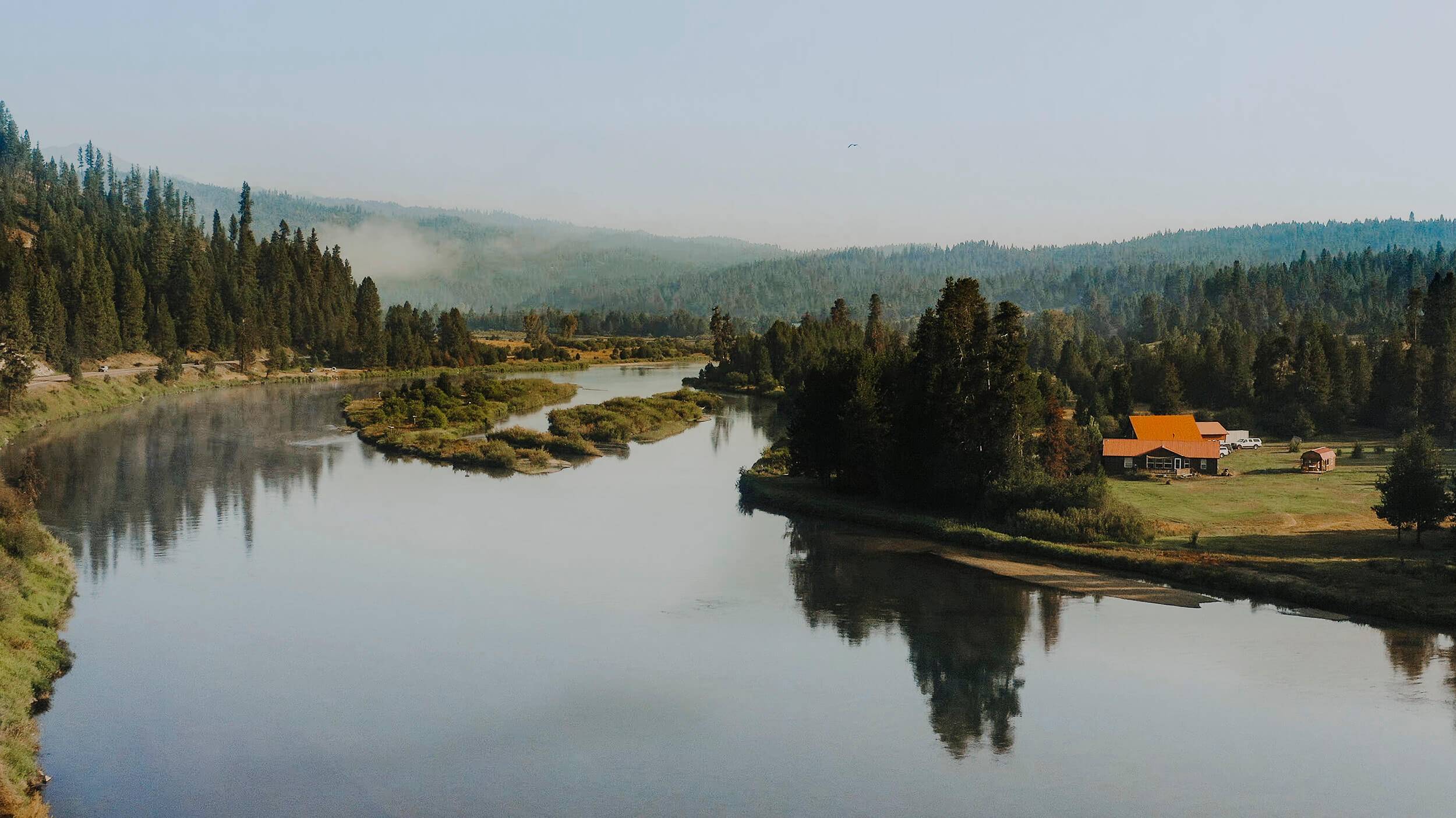 a view of a river lined with trees and a few houses in the distance