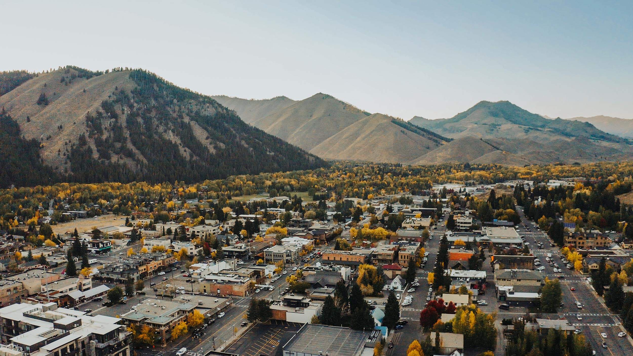 overhead view of a city with green and yellow trees scattered throughout the area, and mountains in the background