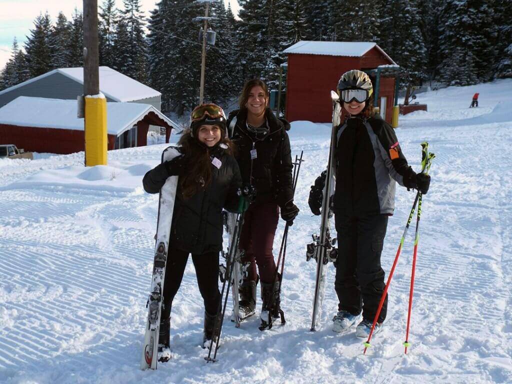 Three people in snow gear stand with ski equipment at Cottonwood Ski Resort.