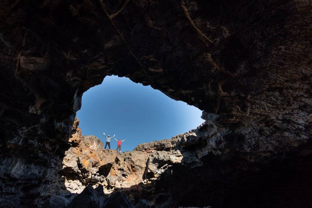 Two people raise their arms at the edge of a lava tube.