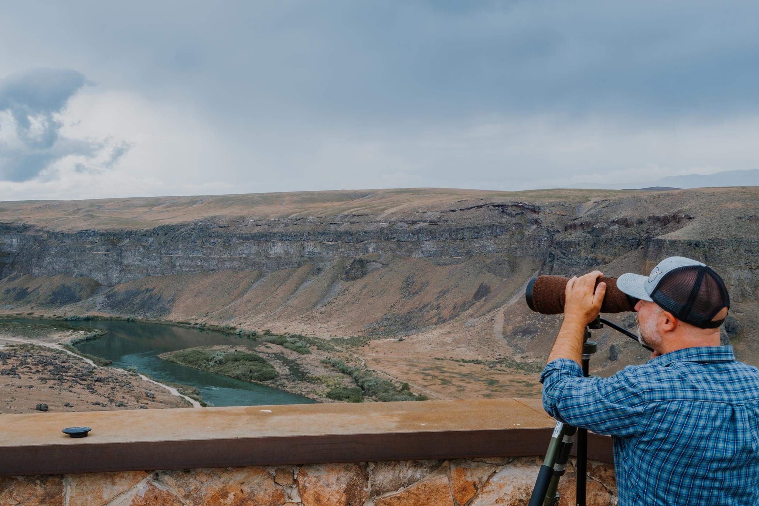 a man looking through a telescope at a river winding through a canyon