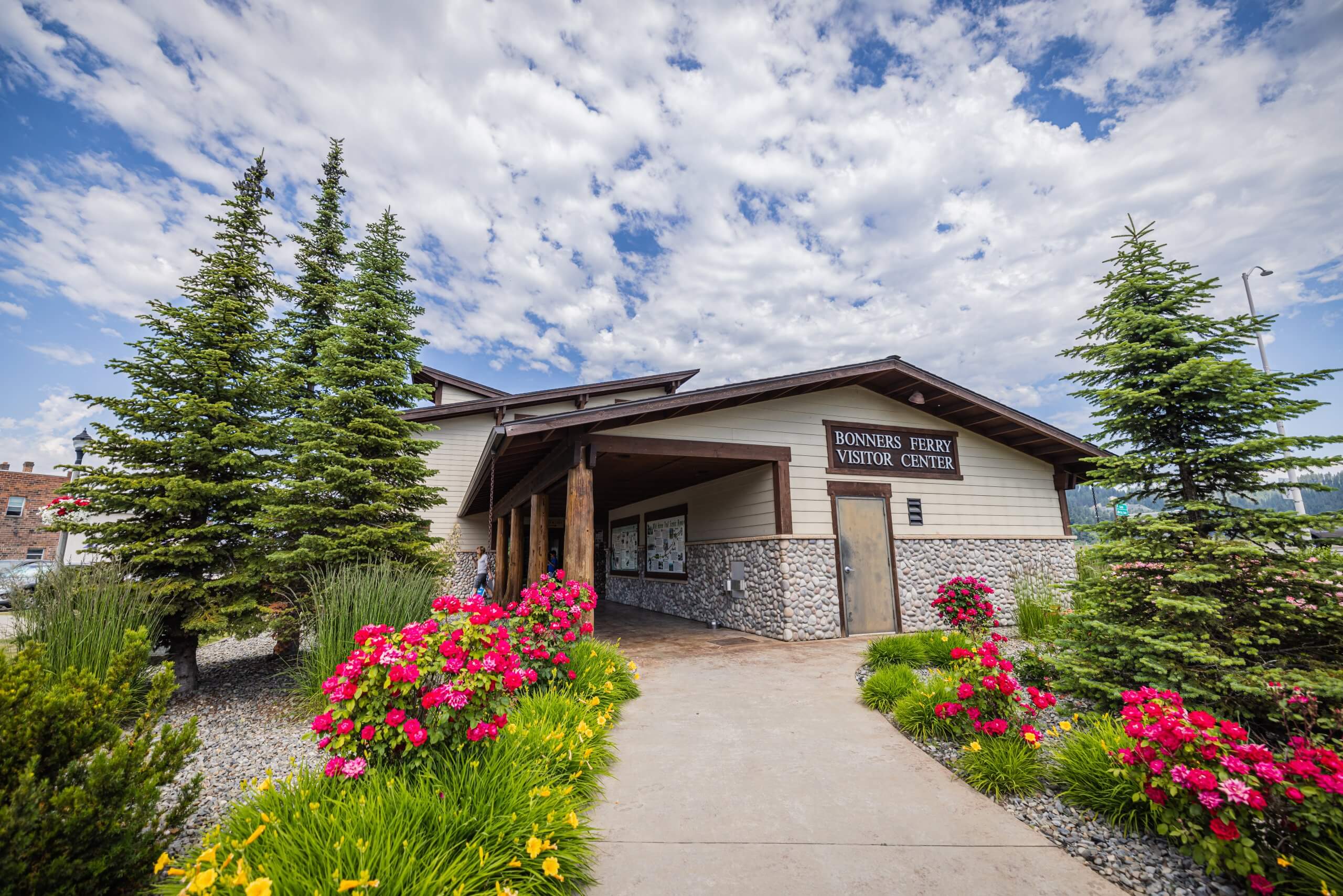 The exterior of the Bonners Ferry Visitor Center surrounded by blooming flowers and green trees.