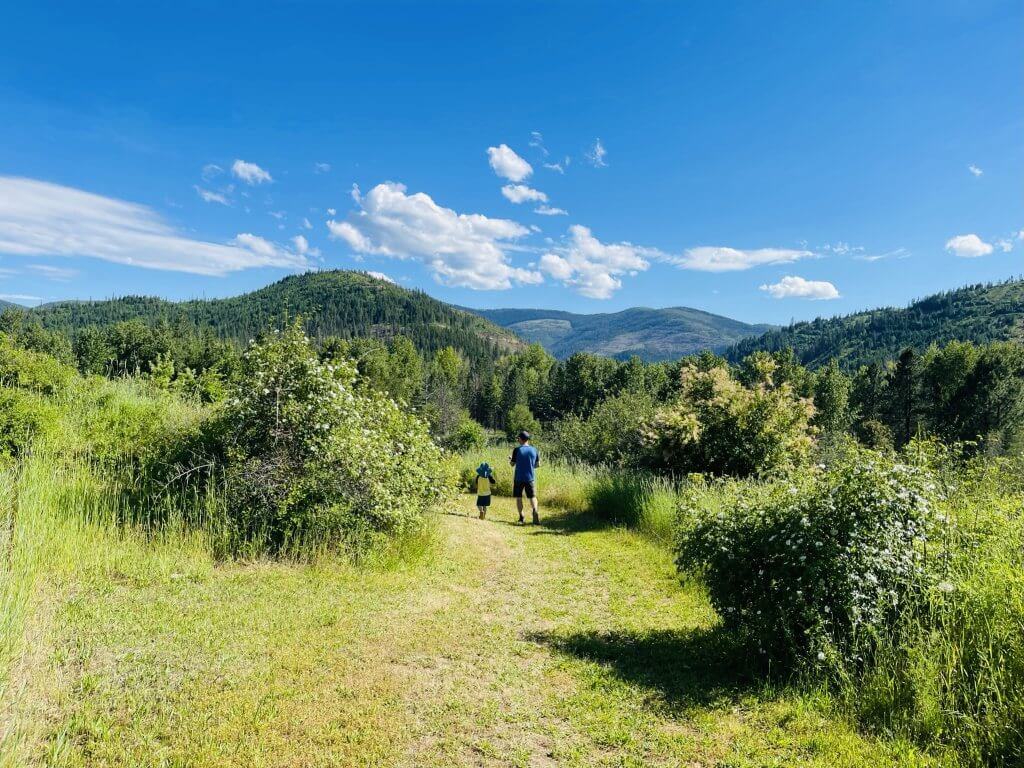 A father and son hold hands while walking on a grassy trail at Coeur d'Alene's Old Mission State Park. 