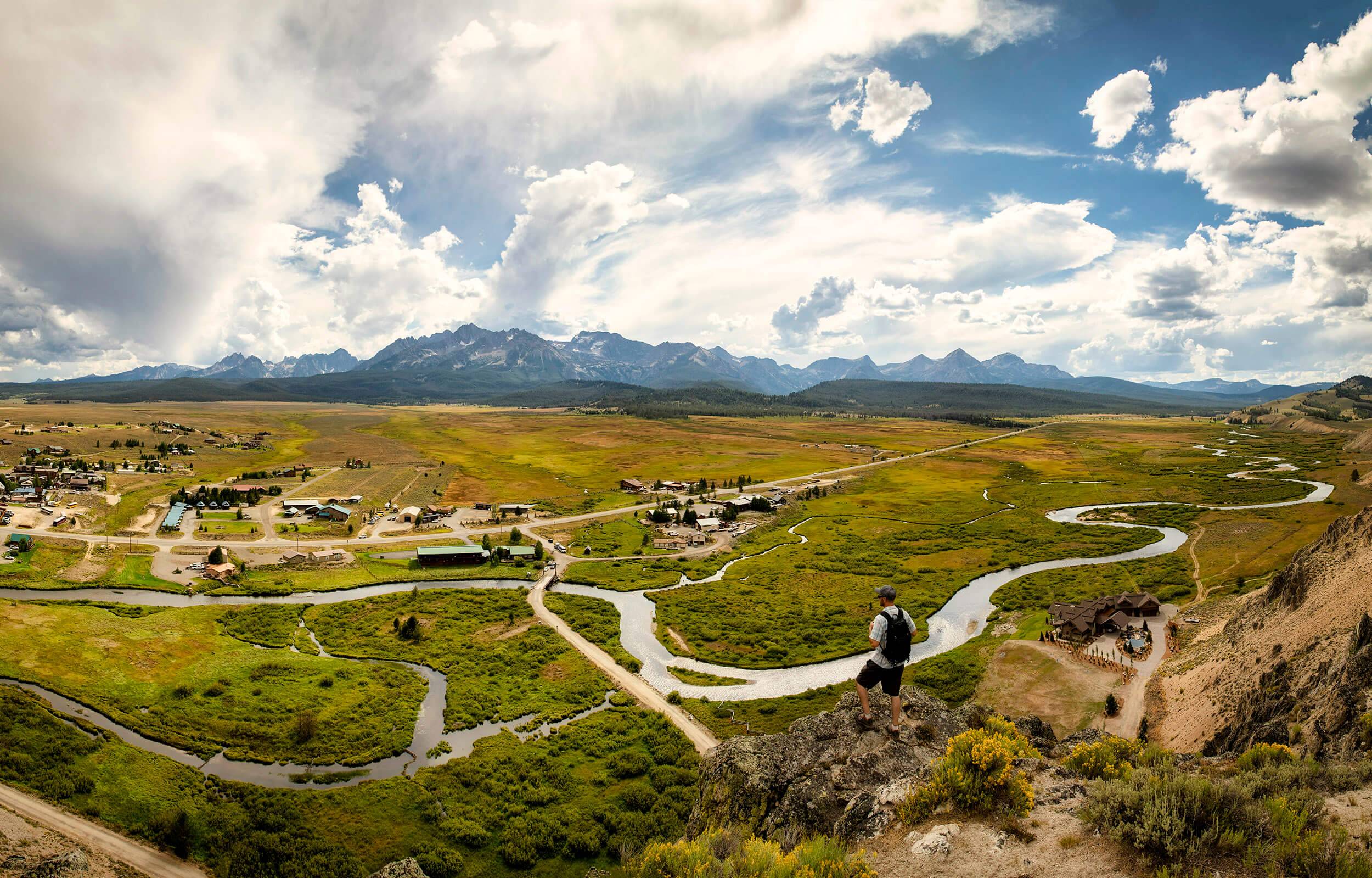 overhead view of a small town and a river running through a grassy landscape, with mountains in the background