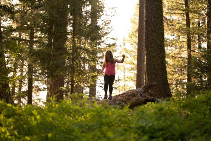 A child walking across a fallen tree in a forest at Ponderosa State Park.