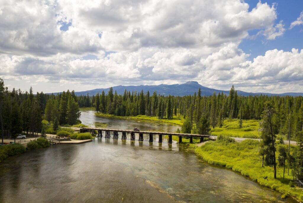 People in an ATV drive across a bridge over water.